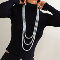 Thumbnail for A woman wearing a black long-sleeve top and a layered pearl necklace with a long chain design.